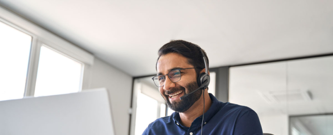 Man with a headset smiling at his laptop