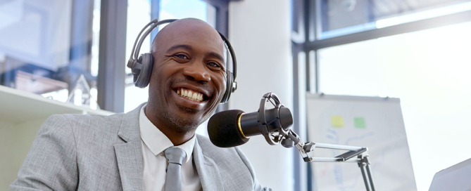 Black CEO wearing headphones at microphone recording podcast.