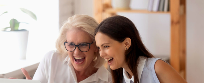 Two female coworkers sitting at a laptop laughing together.