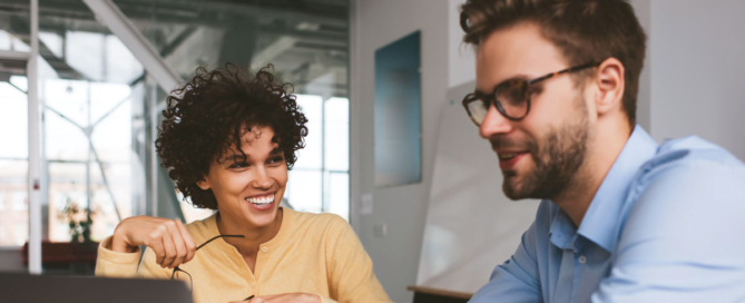 A woman and man discuss as they share a laptop screen.