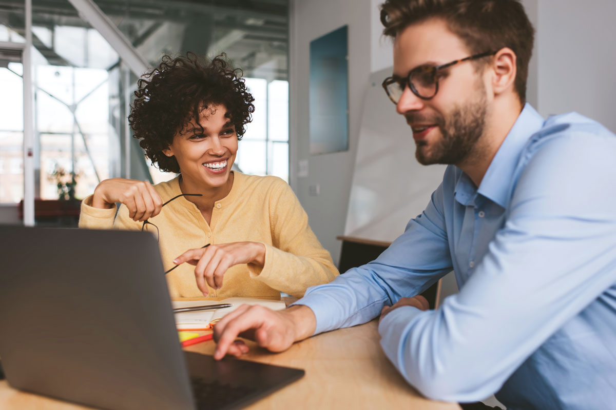 A woman and man discuss as they share a laptop screen.