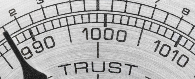 A close up of a metal barometer face reads "Trust Barometer" with the dial pointing to the low end.